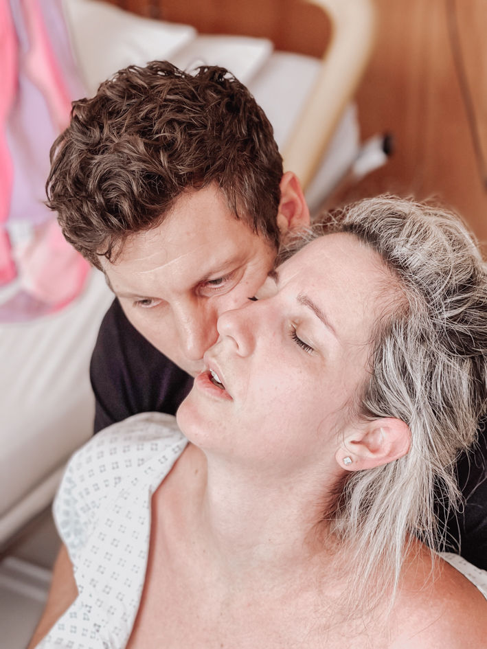Partner küsst eine gebärende Frau auf die Stirn