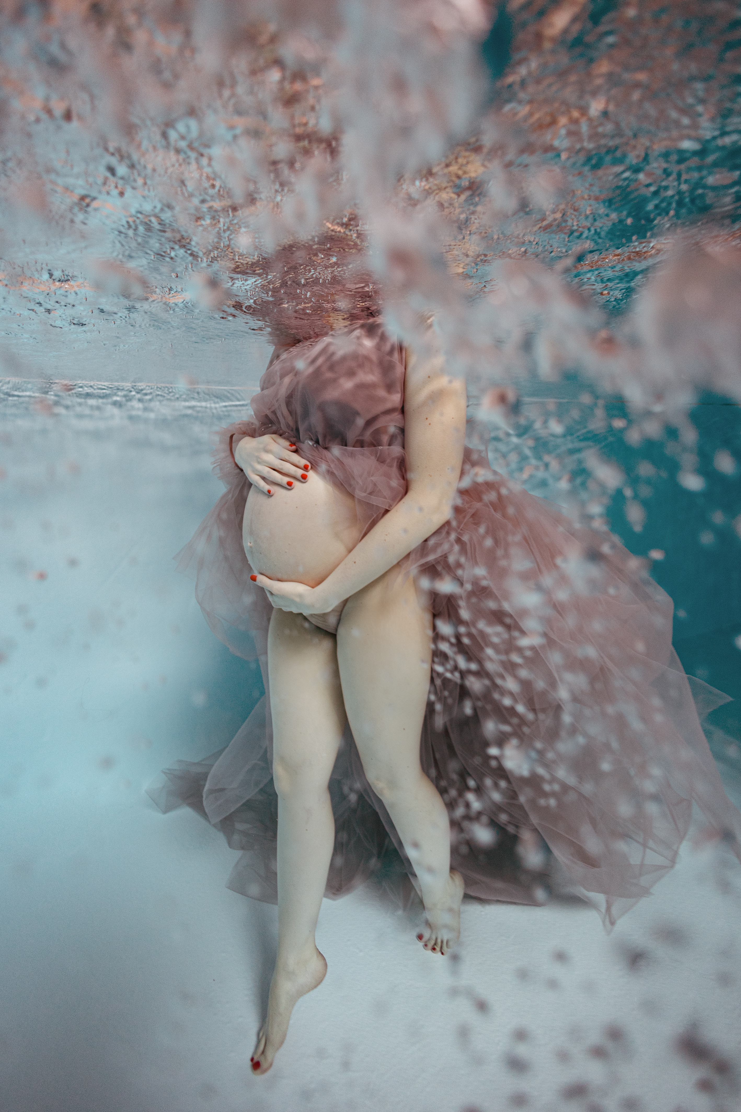 Schwangere Frau im rosafarbenen Kleid unter Wasser